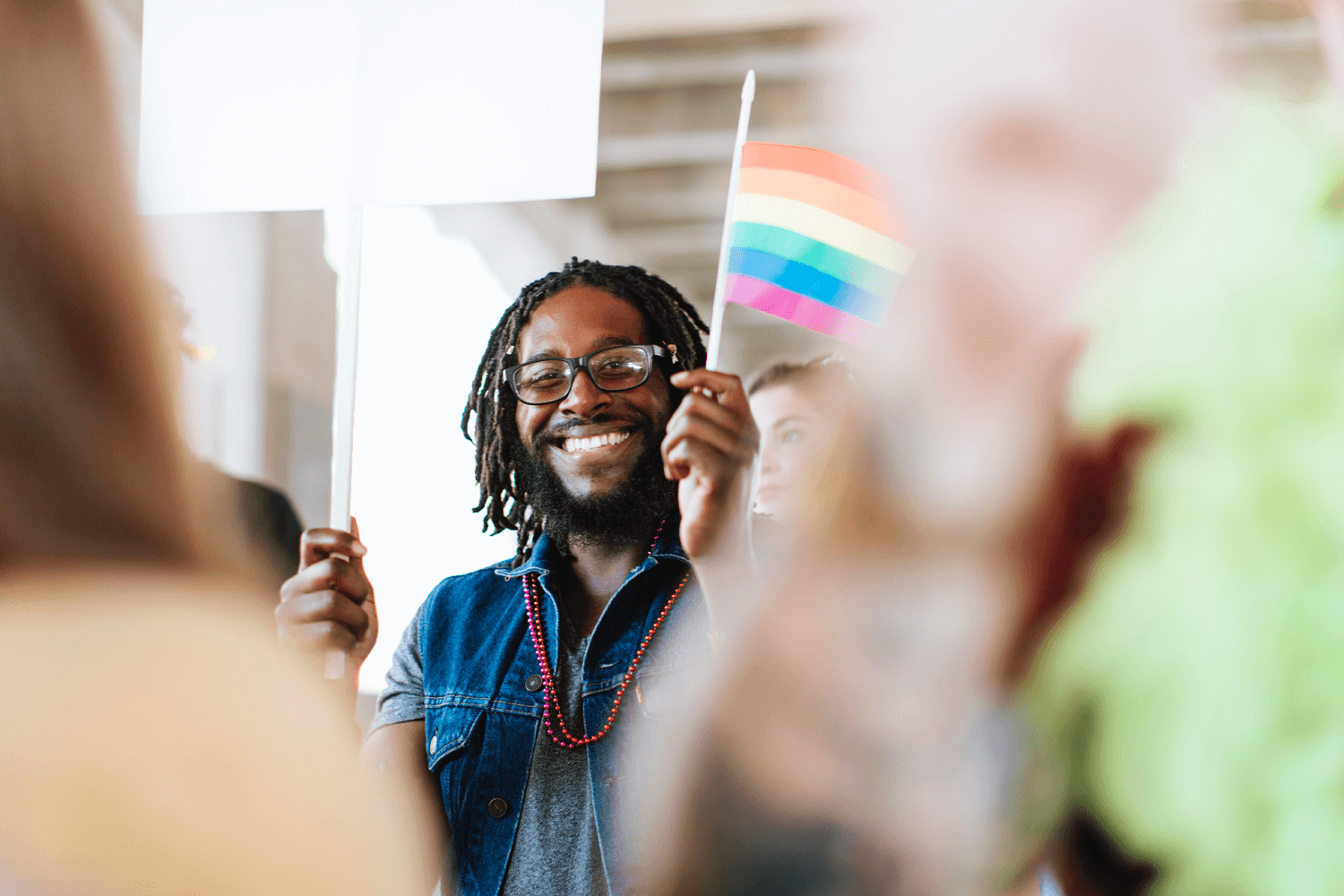 Homem afrodescendente sorrindo e segurando a bandeira do movimento LGBTS